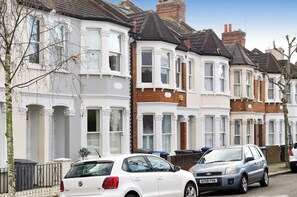 A row of terraced houses with white and red brick facades, bay windows, and a clear sky. - Central London 4BR Queens Park Family Home With Garden (London)