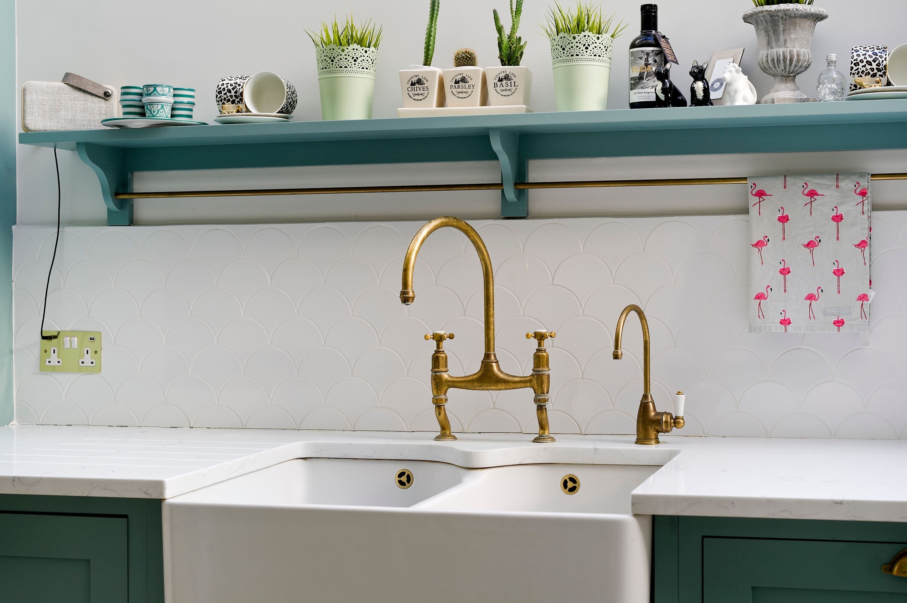 A kitchen with a white sink, a gold faucet, and a teal shelf above the sink holding various items.
