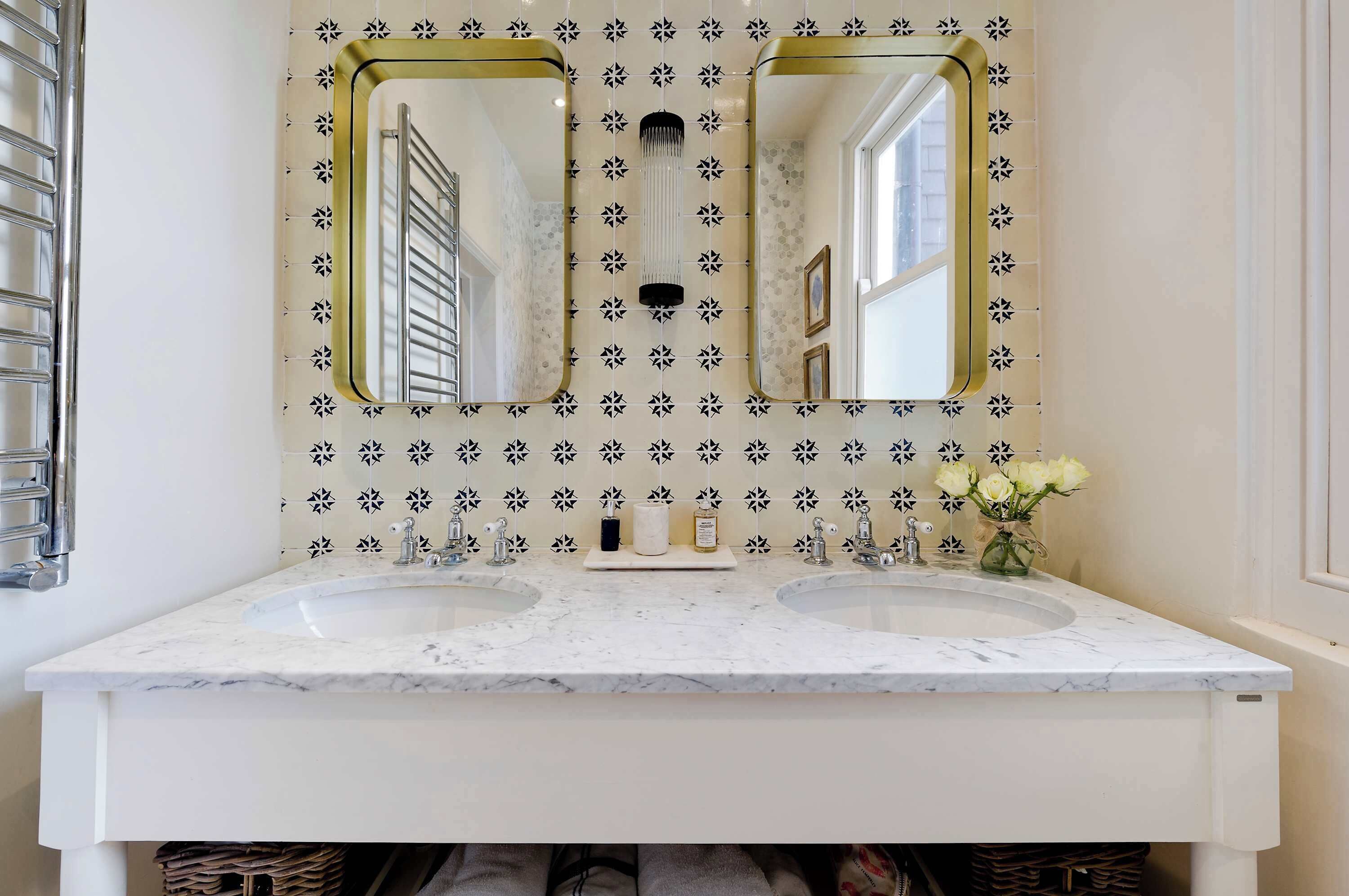 A bathroom with two sinks, a large mirror with a gold frame, and a patterned wall.