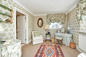 Relax in a charming room with a comfortable armchair, decorative mirror, and floral wallpaper.