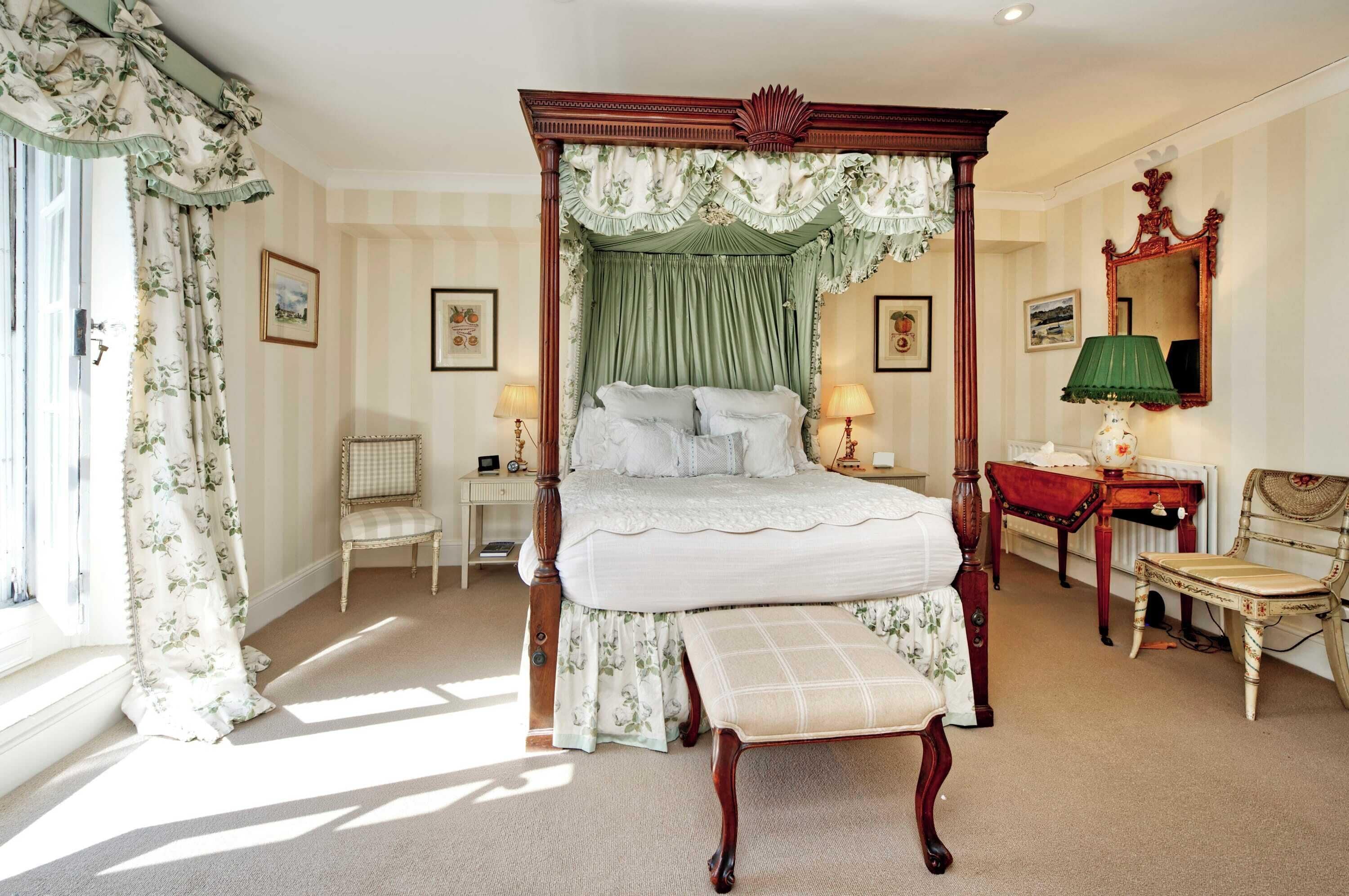 A four-poster bed with a canopy, a bedside table with a lamp, a chair, and a mirror on the wall.