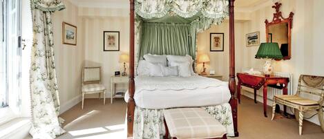 A four-poster bed with a canopy, a bedside table with a lamp, a chair, and a mirror on the wall.