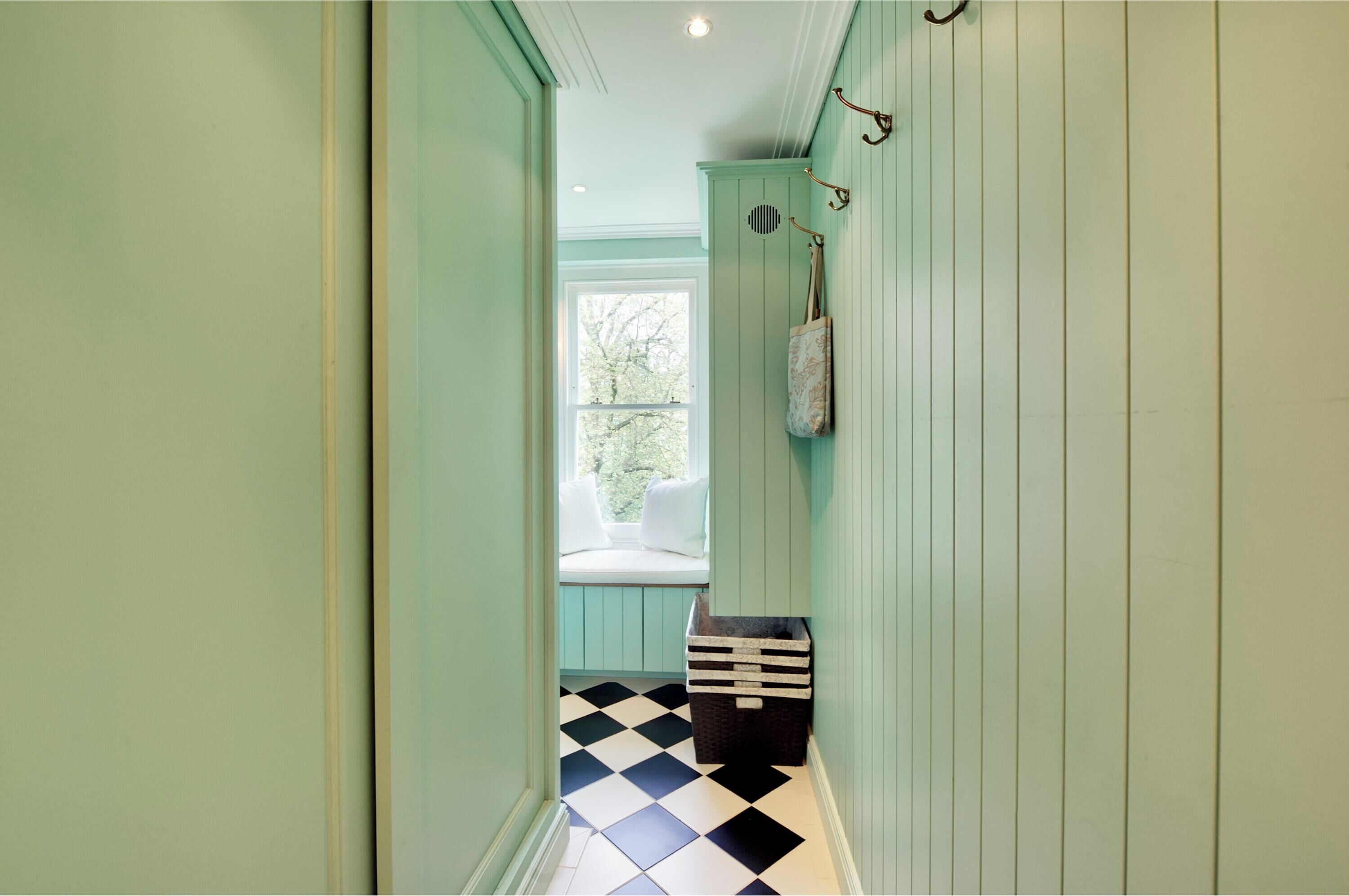 A hallway with light green walls, a checkered floor, a window with a view of trees, and a small storage box.