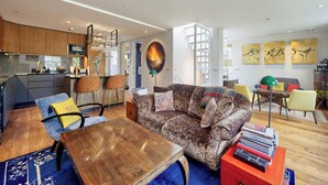 A modern living room with a sofa, coffee table, and chairs. There is a kitchen area with cabinets and a dining table with chairs. - Stunning 2 Bedroom Apartment in Little Venice West London (London)