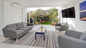 A modern living room with grey sofas, a striped rug, and a flat-screen TV mounted on the wall. - Spacious 4 Bed House, Battersea (London)