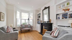 A living room with two grey sofas, a striped armchair, a fireplace, and a bookshelf with books and decorative items. - Spacious 4 Bed House, Battersea (London)