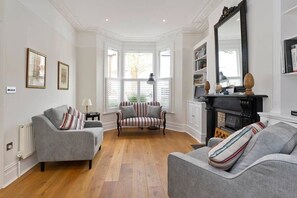 A room with a fireplace, a sofa, a striped armchair, and a large mirror. - Spacious 4 Bed House, Battersea (London)