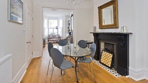 A dining area with a glass table and chairs, a fireplace, and a chandelier. - Spacious 4 Bed House, Battersea (London)