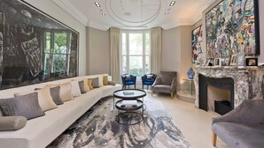 A modern living room with a large window, a fireplace, and a large abstract painting. - 7bed Notting Hill W/garden, Games Room & Parking (London)