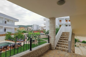A balcony with a stone staircase, a pool, and a view of surrounding buildings. - Casa Del Mar (Ksamil)