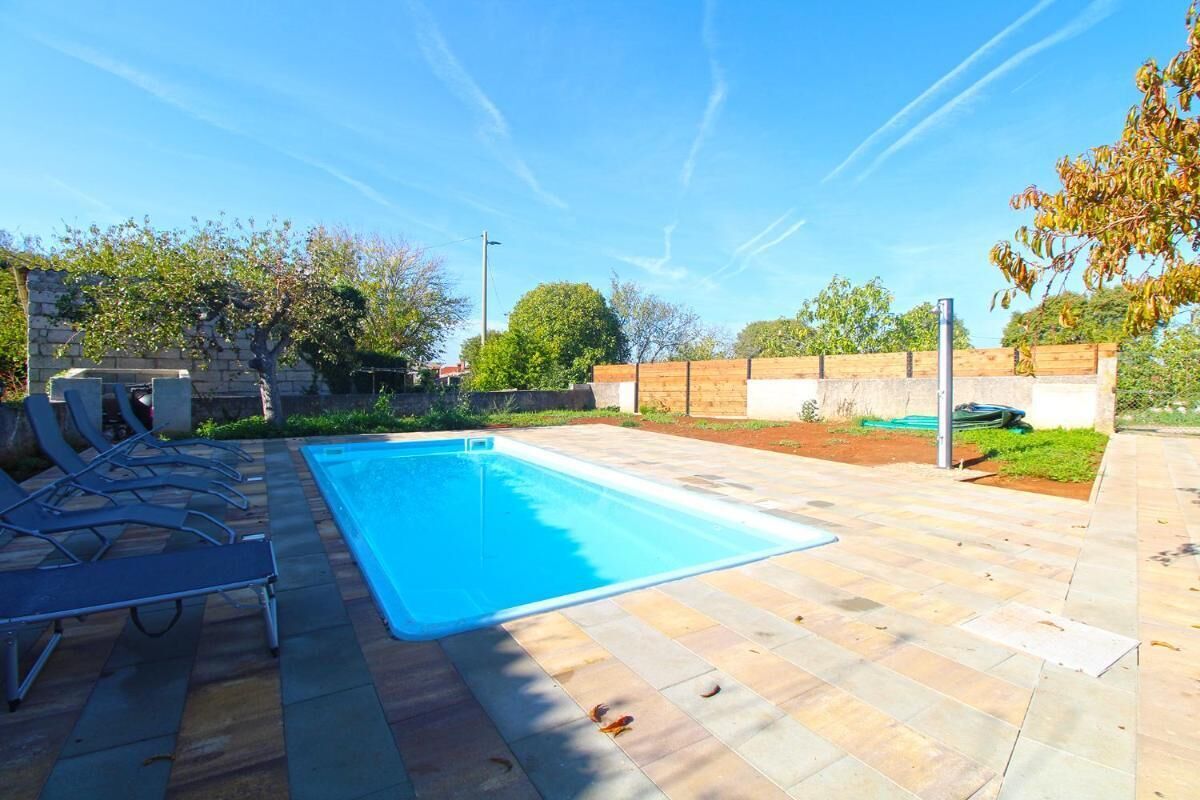 Une piscine rectangulaire, bordée d’une terrasse carrelée et entourée d’un mur de pierre et d’une clôture en bois.