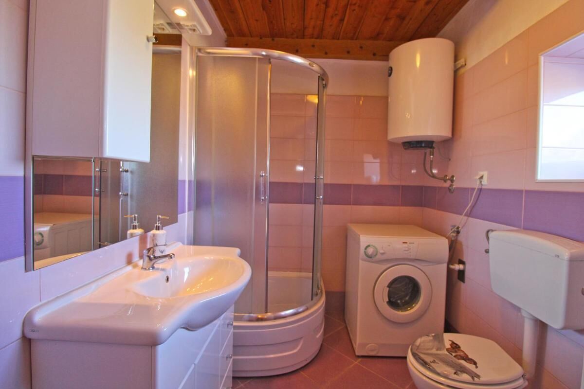 A compact bathroom with a glass-enclosed shower, a sink, a washing machine, and a toilet.