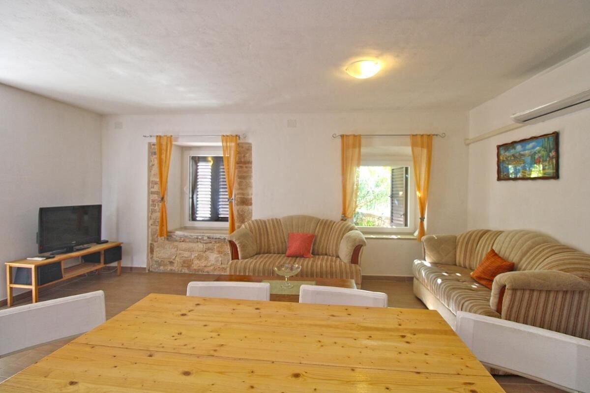 Un salon avec une table à manger en bois, deux canapés, un téléviseur et un mur en pierre.
