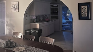 A dining area with a round table, chairs, and a ceiling fan. There is a kitchen visible through an archway with cabinets and appliances. - Spacious country oasis:Swim,BBQ, Attend Weddings!Close to venues in Hill Country (Austin)