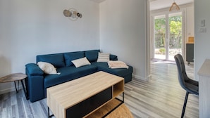 Un moderno salón con un sofá azul, una mesa de centro de madera y vistas a un área exterior a través de un ventanal.