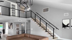 Un amplio salón con un sofá seccional de cuero marrón, una mesa de centro negra y una escalera de madera con barandales negros.