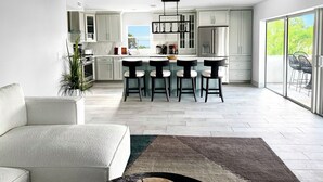 Cocina moderna con armarios blancos, una isla central con taburetes y un amplio ventanal corredera que da a un balcón.