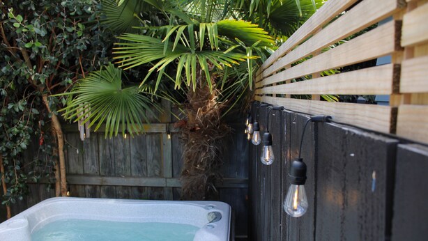 A hot tub with a wooden fence and a palm tree in the background.