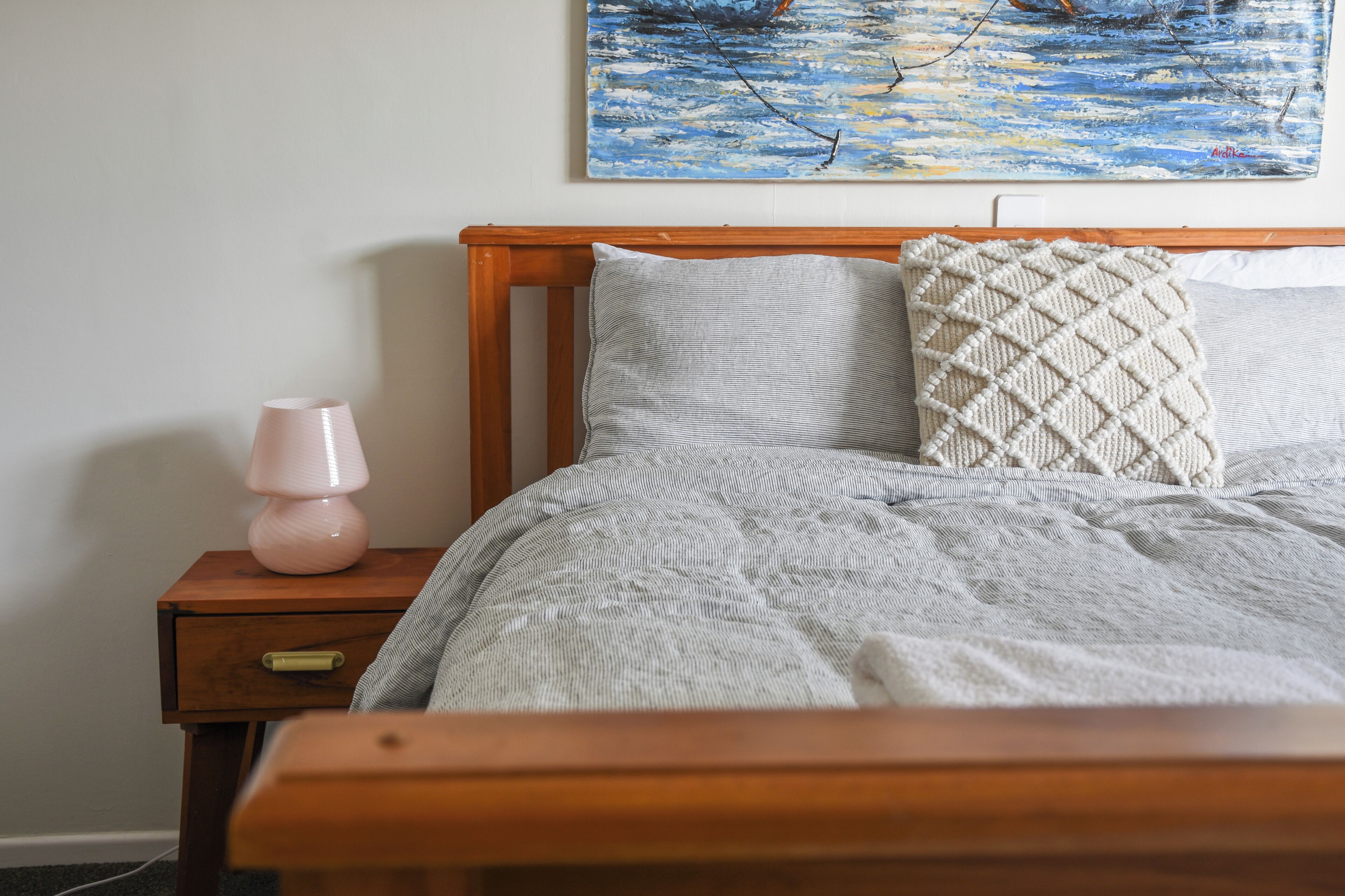 Un lit bien fait, avec une couverture à motifs et des oreillers, une lampe de chevet et un tableau accroché au mur.