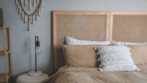 A bed with a rattan headboard, a bedside lamp, and a white wall with a macramé decoration.