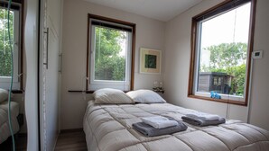 A bedroom with a bed, two windows, a picture on the wall, and a view of trees outside. - Jamies Cottage Warmenhuizen (Warmenhuizen)