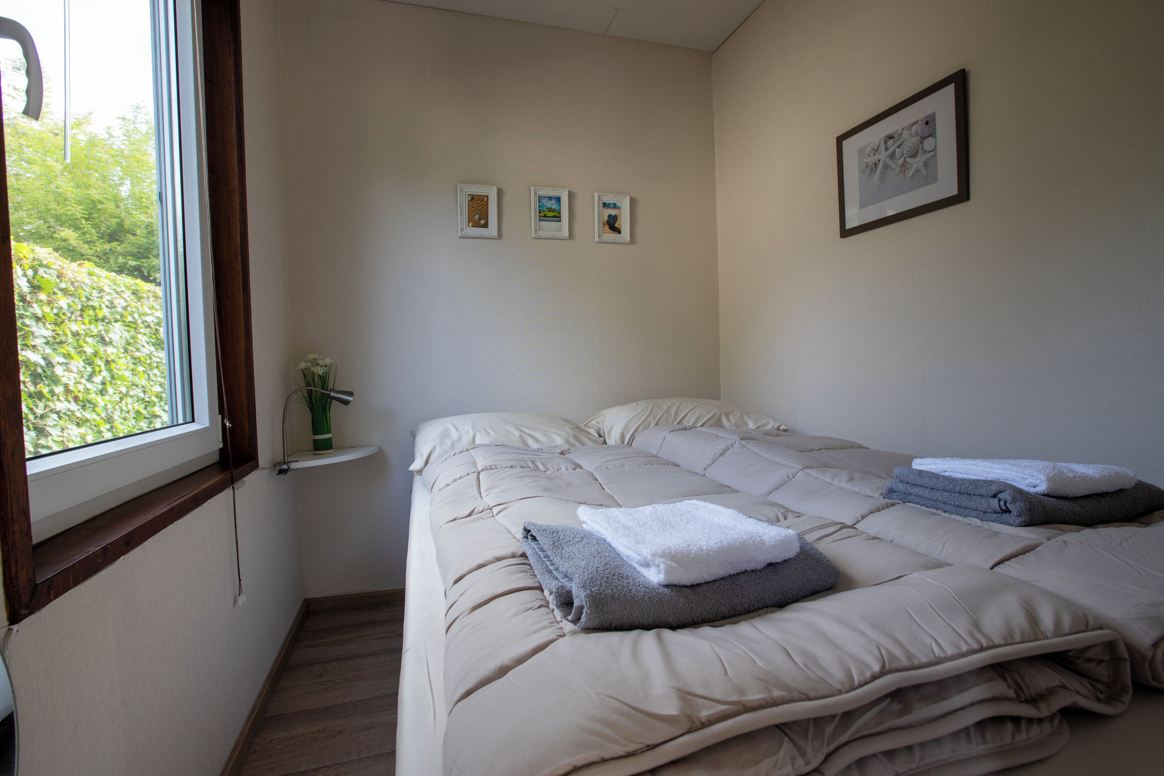 Une chambre avec un grand lit, une petite table de chevet et trois tableaux encadrés accrochés au mur.