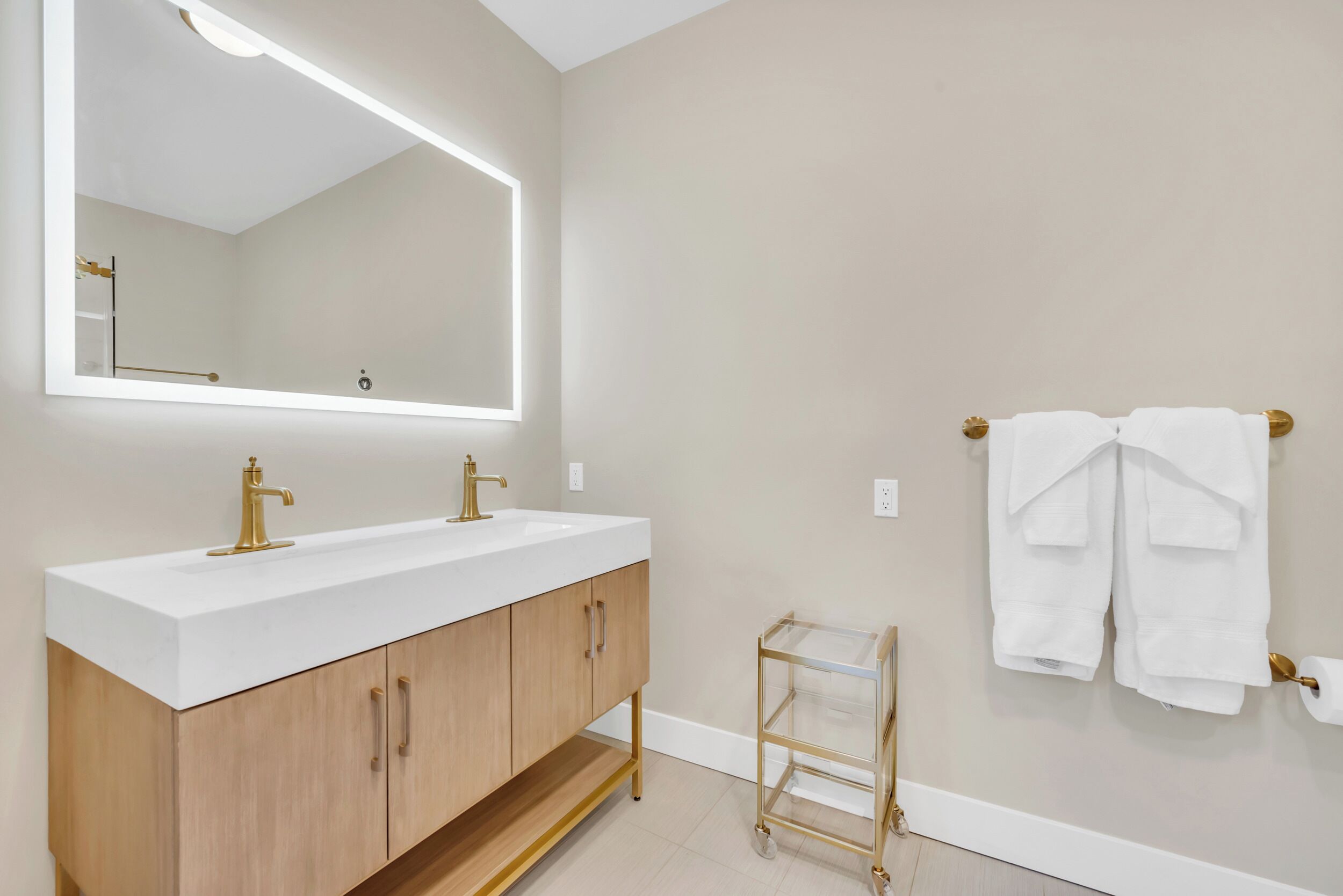 A bathroom with a large mirror, two sinks, a vanity with wooden cabinets, and a towel rack with towels.