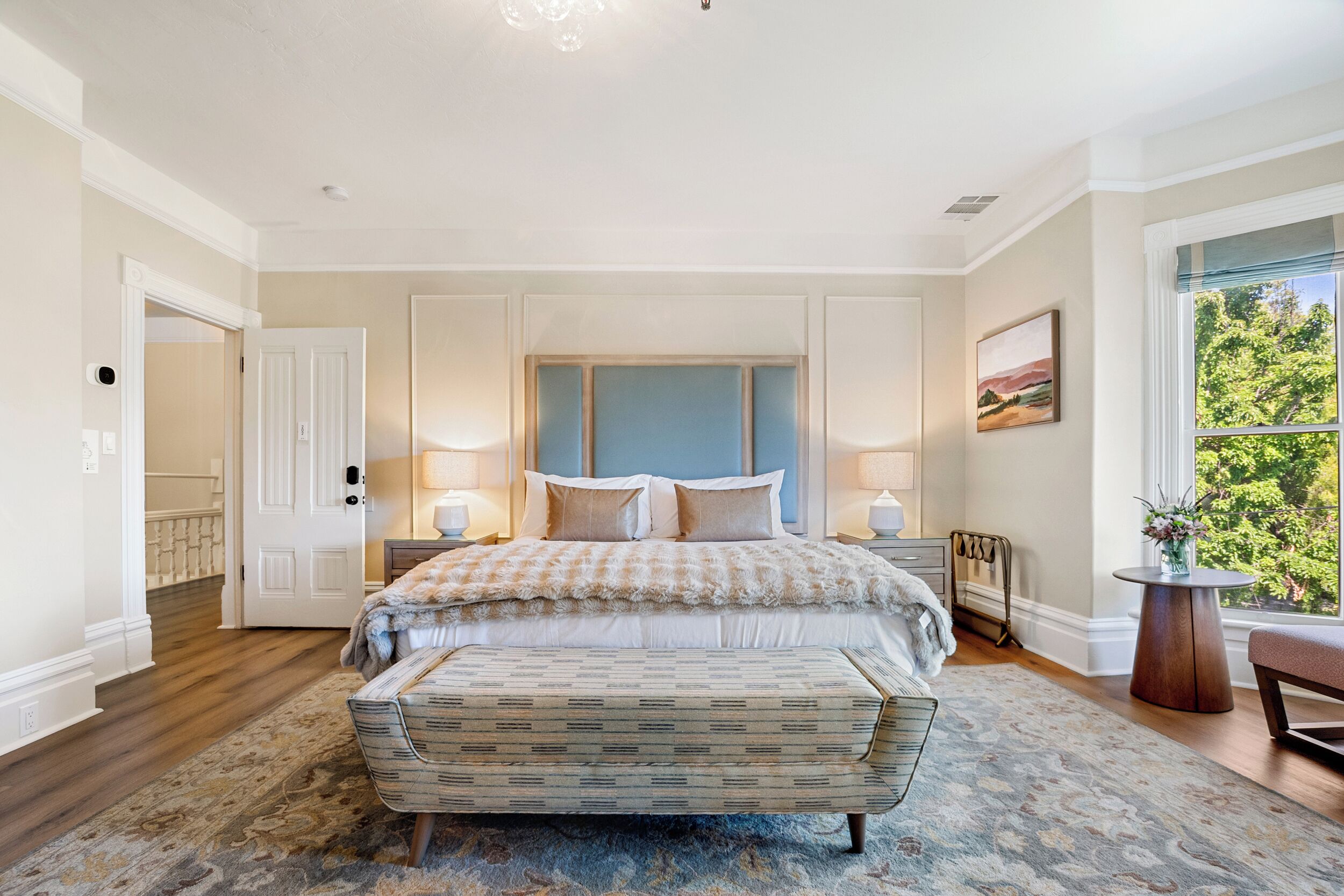 A bedroom with a large bed, a bench, a nightstand, and a window with a view.