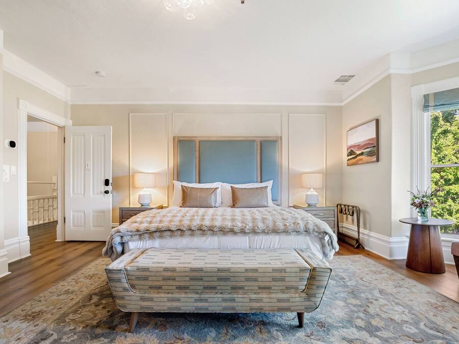 A bedroom with a large bed, a bench, a nightstand, and a window with a view.