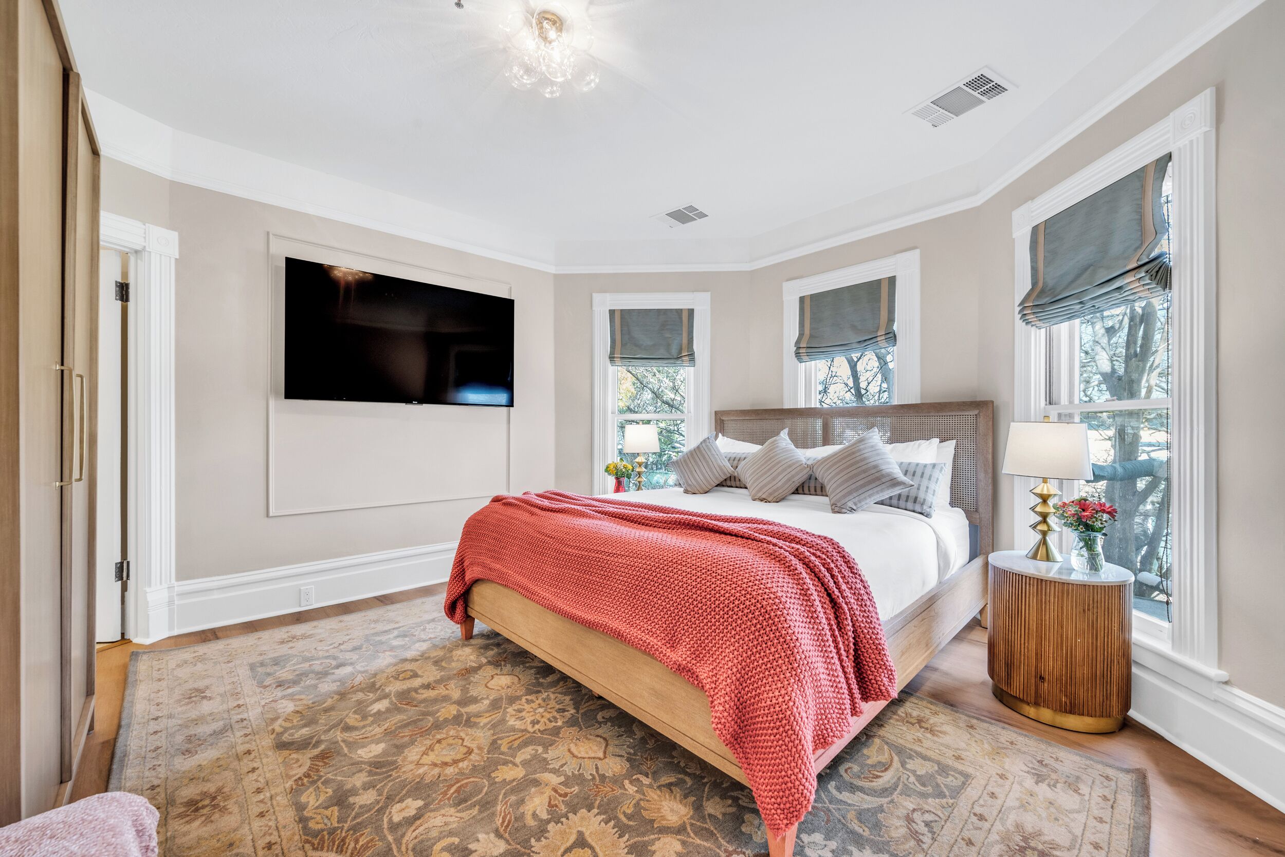 Un dormitorio con cama, televisor montado en la pared y ventana con vista a árboles.