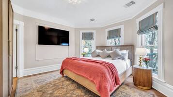 Un dormitorio con cama, televisor montado en la pared y ventana con vista a árboles.