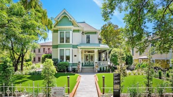Ein zweistöckiges Haus mit grüner und weißer Fassade, einer Veranda und einem gepflegten Garten.