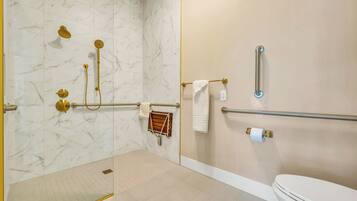 A bathroom with a marble wall, a toilet, a shower with gold fixtures, and a grab bar.