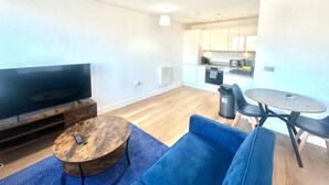 A modern living room with a flat-screen TV, a wooden coffee table, a blue sofa, and a small dining table with chairs. - Up to 40 Percent Off Old Trafford Modern Apartment (Manchester)