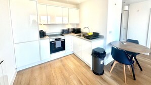 A modern kitchen with white cabinets, a built-in oven, a sink, and a dining area with a wooden table and chairs. - Up to 40 Percent Off Old Trafford Modern Apartment (Manchester)