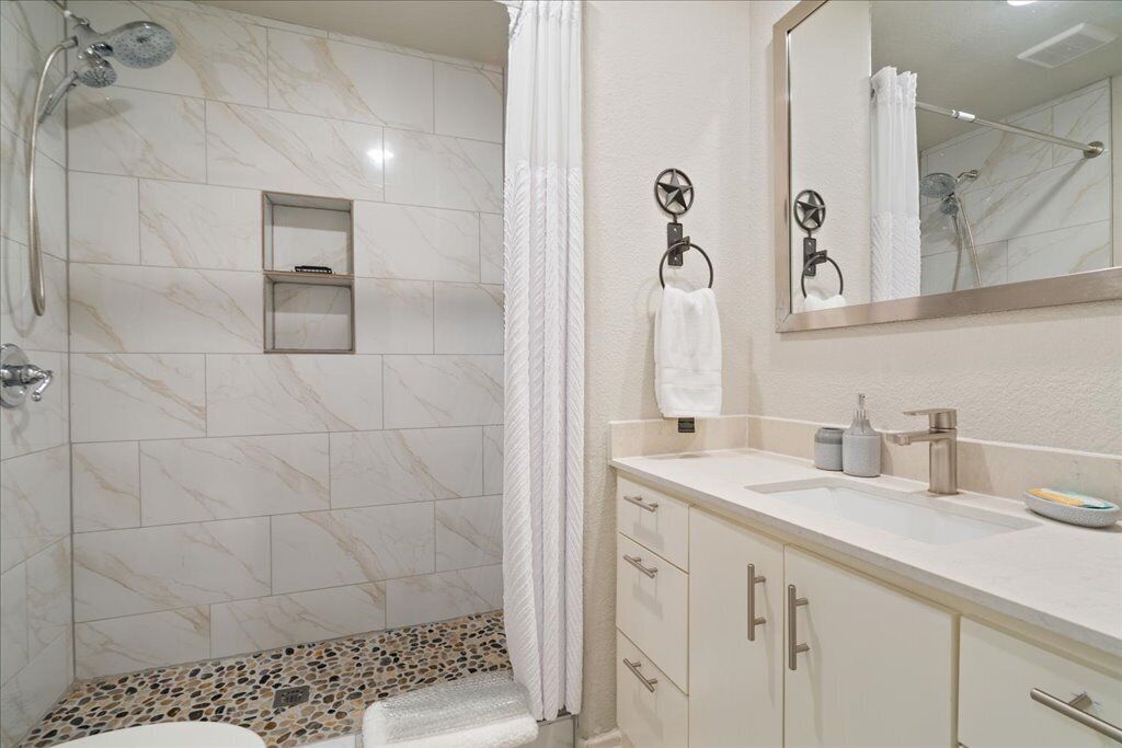 A modern bathroom with a shower, a vanity with a sink, and a mirror.