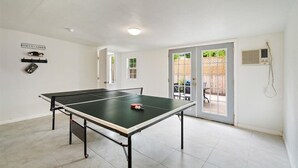 A ping pong table in a room with white walls, a ceiling light, and a door leading to an outdoor area with a patio. - SoCo Austin Home & Cowboy Charm (Austin)