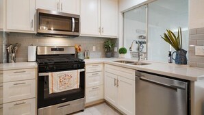 A modern kitchen with stainless steel appliances, white cabinetry, and a large window. - SoCo Austin Home & Cowboy Charm (Austin)
