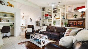 A modern living room with a leather sofa, white coffee table, and a bookshelf filled with books and decorative items. - SoCo Austin Home & Cowboy Charm (Austin)