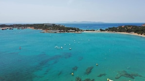 Vista aérea de una zona costera con aguas turquesas cristalinas, una playa arenosa y una pequeña isla con edificios.