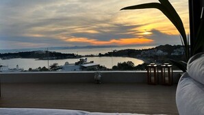 Vista al atardecer desde un balcón con piso de madera, una escultura de piedra y una fila de faroles.