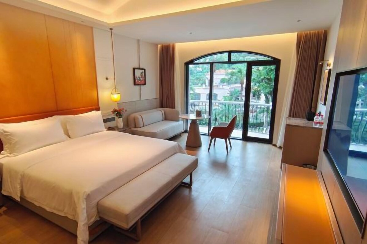 A hotel room with a bed, a sofa, a TV, and a balcony with a view.