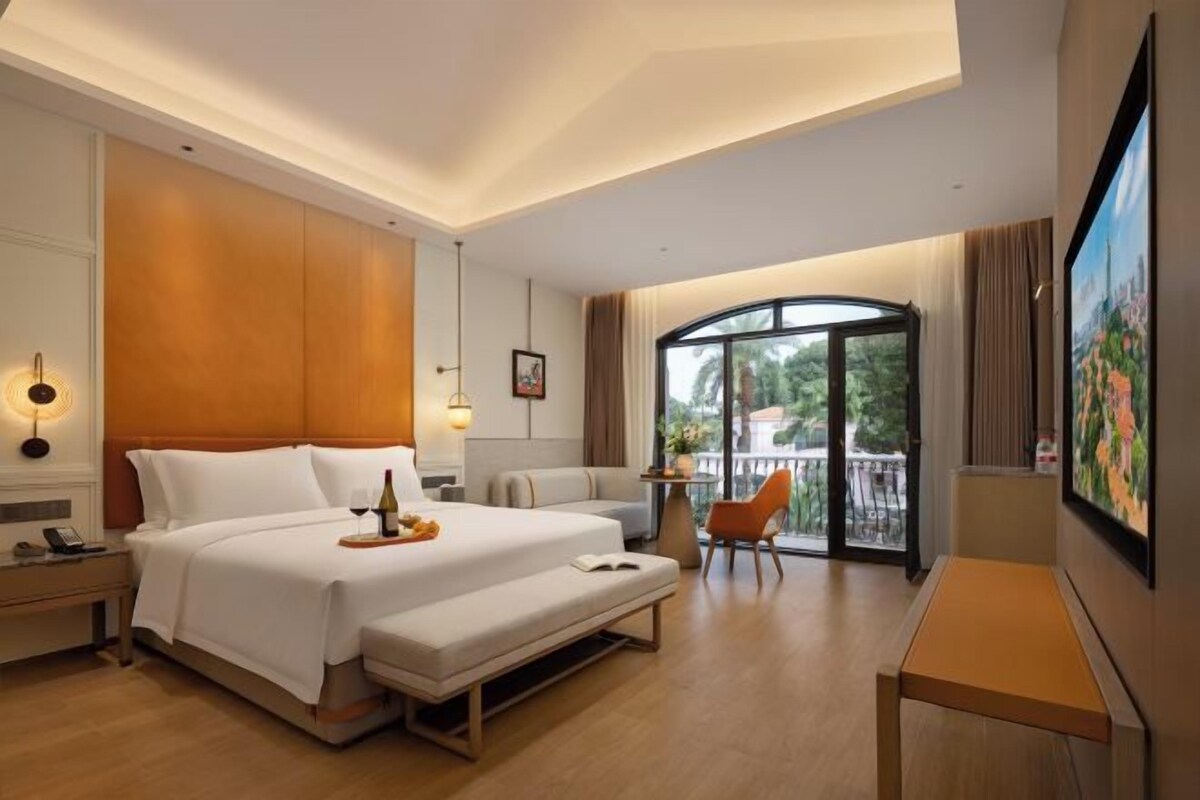 A hotel room with a large bed, a bench, a desk, and a balcony with a view.