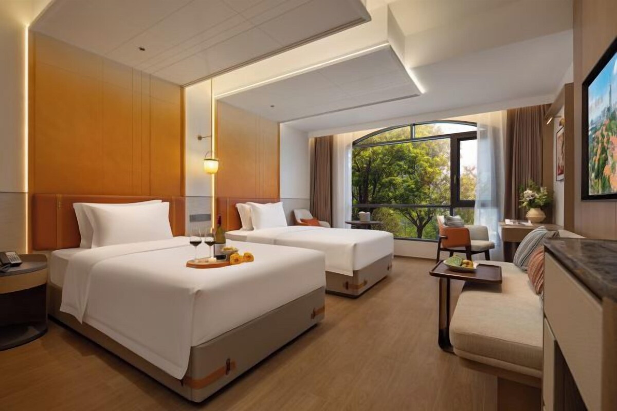 A hotel room with two beds, a sofa, a small table, and a large window with a view.