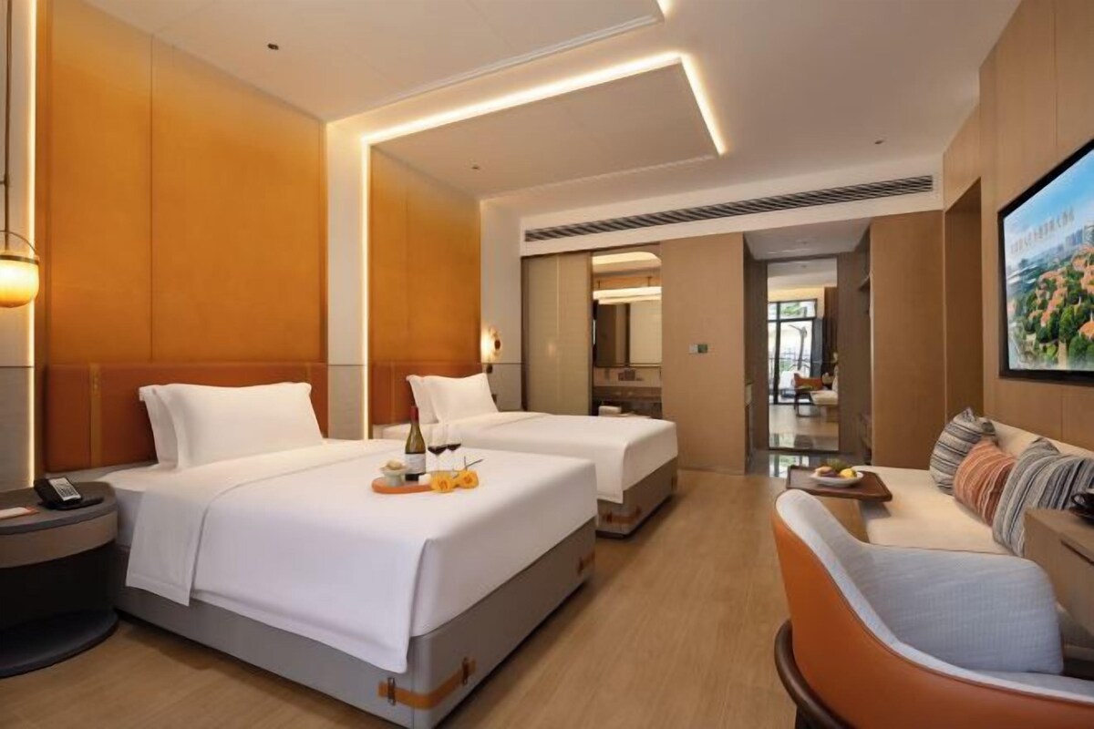 A hotel room with two beds, a sofa, a TV, and a dining table.