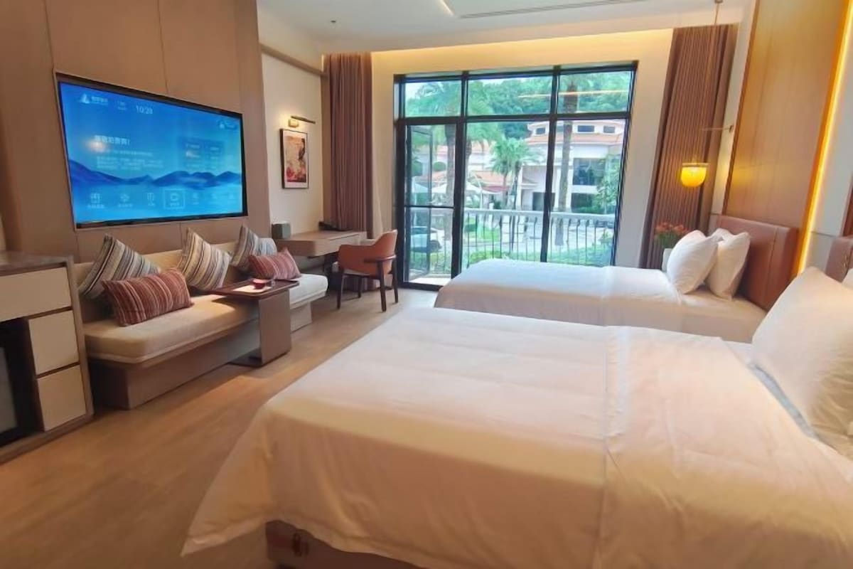 A hotel room with two beds, a desk, a chair, and a TV.