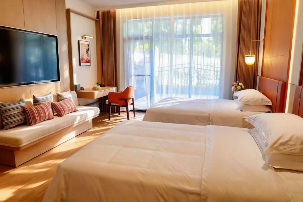 A hotel room with two beds, a sofa, a desk, and a TV.