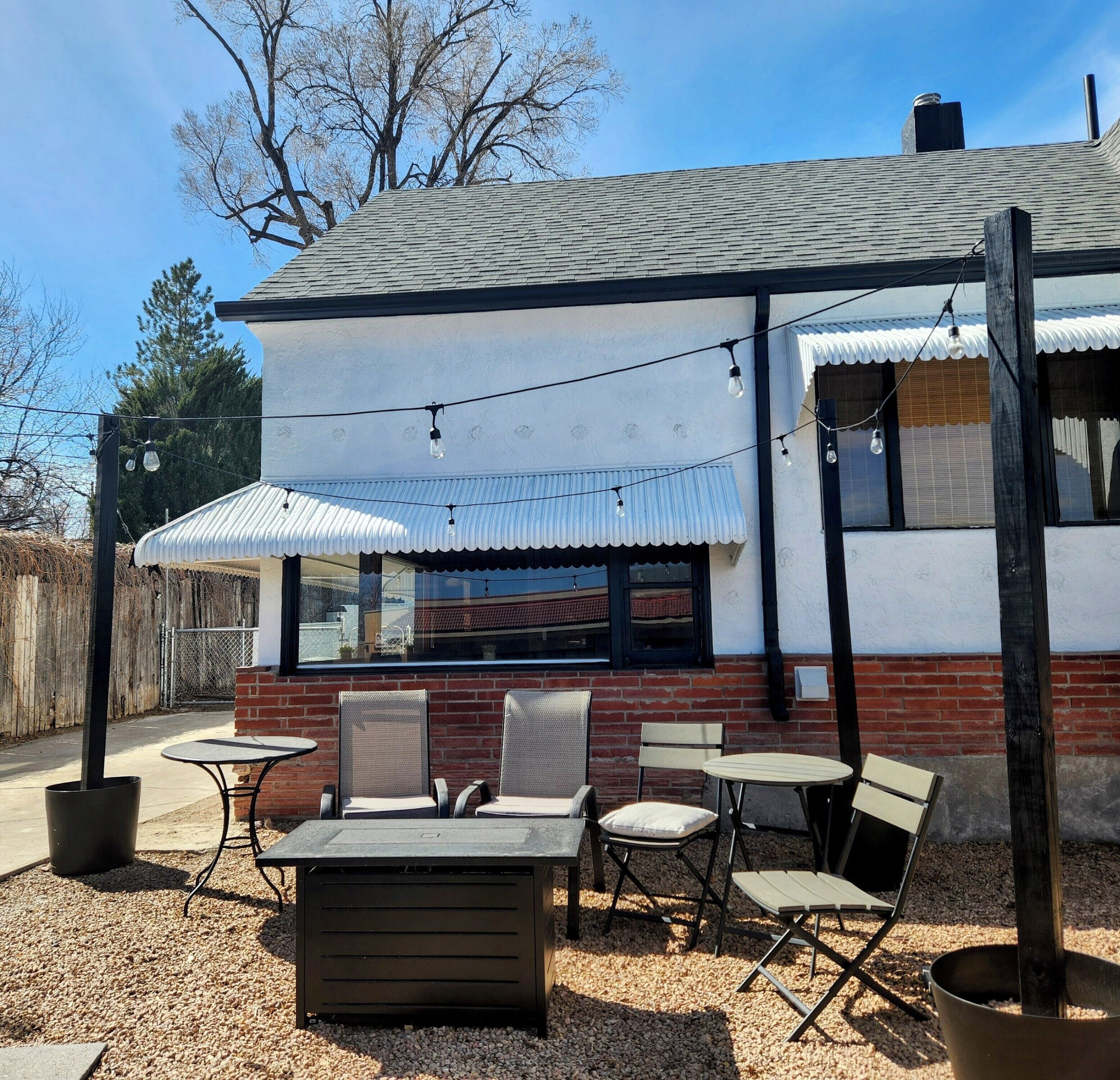 An outdoor seating area with tables and chairs, a brick wall, and string lights.