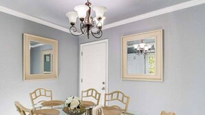 A dining area with a glass table surrounded by wicker chairs, a chandelier, and framed mirrors on the walls. - Cozy 3-Bedroom Home – Sleeps 6 (Tulsa)