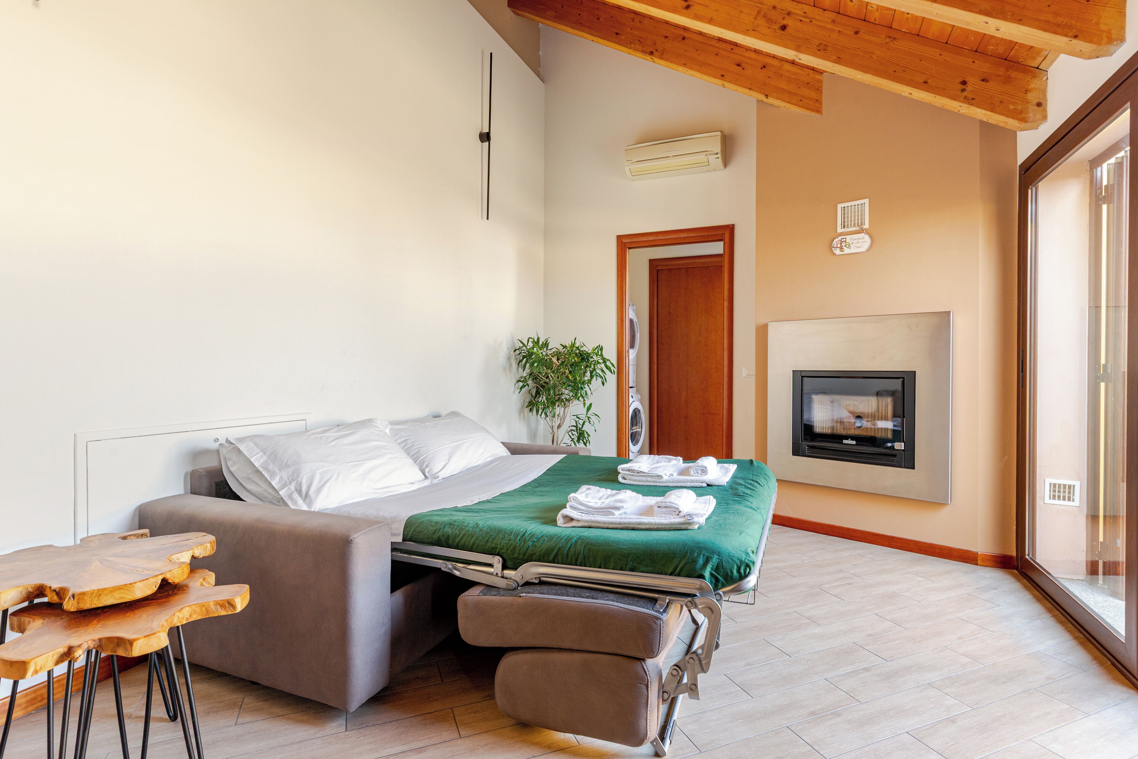 Un dormitorio moderno con un sofá cama, una mesita, una manta verde y una chimenea.